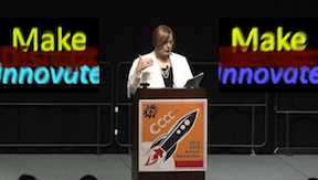 screenshot from the video with Joyce at a podium and the blurry words Make Disrupt Innovate in side boxes on both side of her