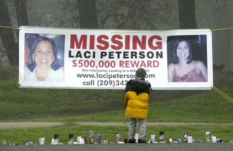 large sign reading: Missing: Laci Peterson, $500,000 award; child stands looking at sign; row of candles in front of sign