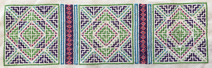 A cross-stitch using a pattern in blues, greens, purples, and pinks