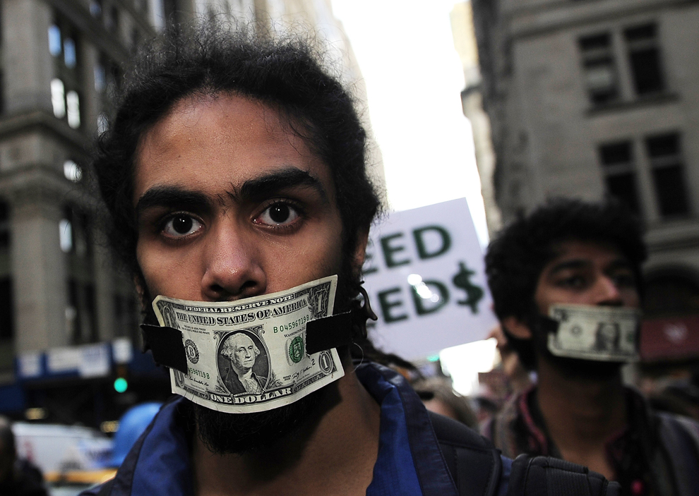 Members of Occupy Wall Street protest with dollar bills taped over their mouths. Photo taken in New York on October 15, 2011. Credit to Emmanuel Dunand/AFP/Getty Images.