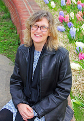 photo of Arduser looking up at the camera. She's wearing a leather jacket and glasses and looking up at the camera. There are flowers in the background.