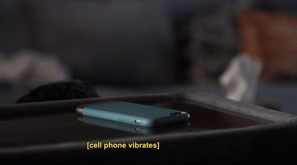 An animated gif from an episode of Pretty Little Liars. A young woman sits on her couch looking at her phone as the text message she is reading is visualized on the screen: 'When the pigs come calling, you better not squeal about me.' The pigs are two emoji pig characters, and a bomb emoji and broken heart emoji are included at the end of the on-screen text message too. 
