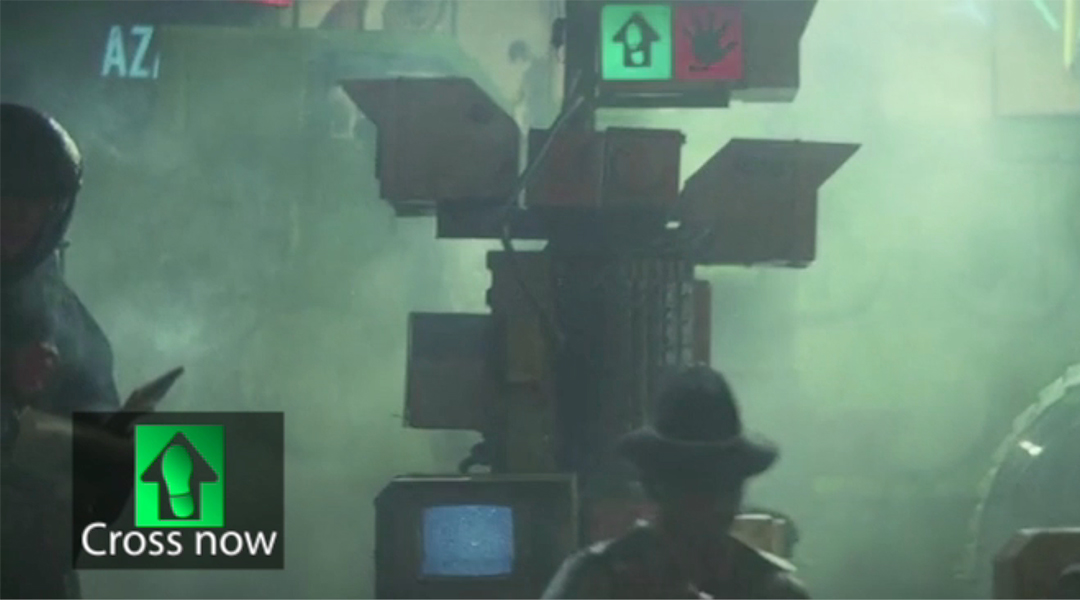 A frame from Blade Runner featuring a street scene with cross walk signal