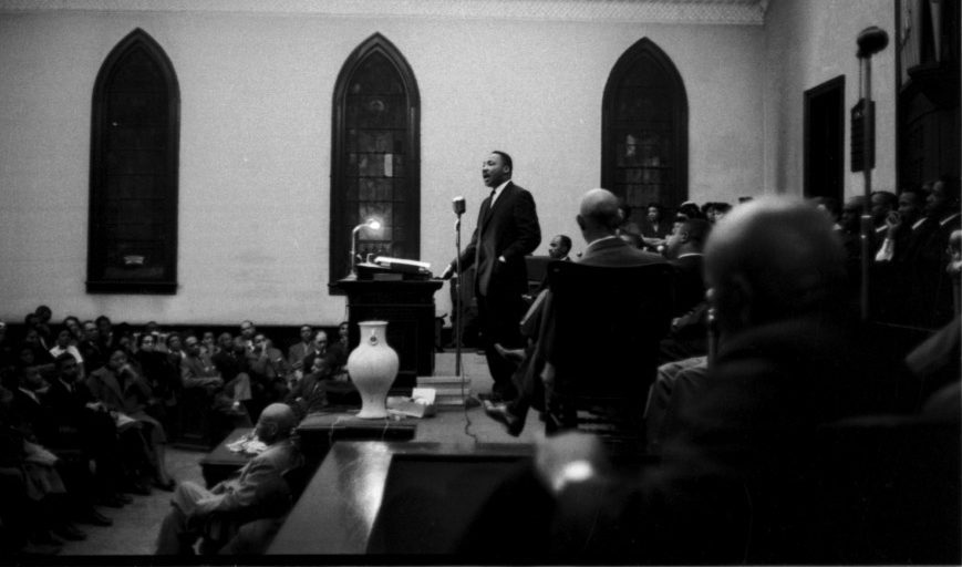 Martin Luther King at a podium delivering a speech in a church; black and white
