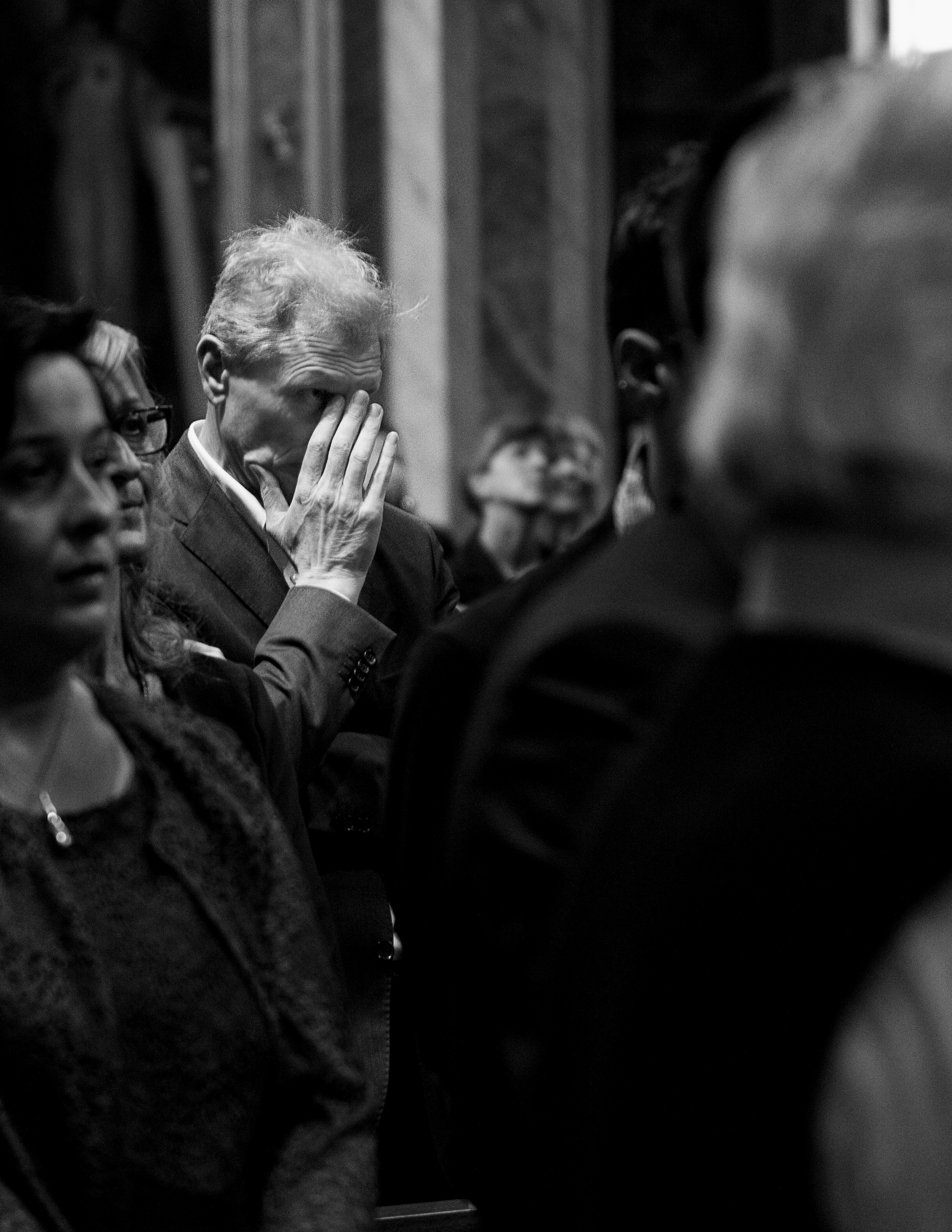 A man wiping a tear from his eye sits in a crowded church congregation