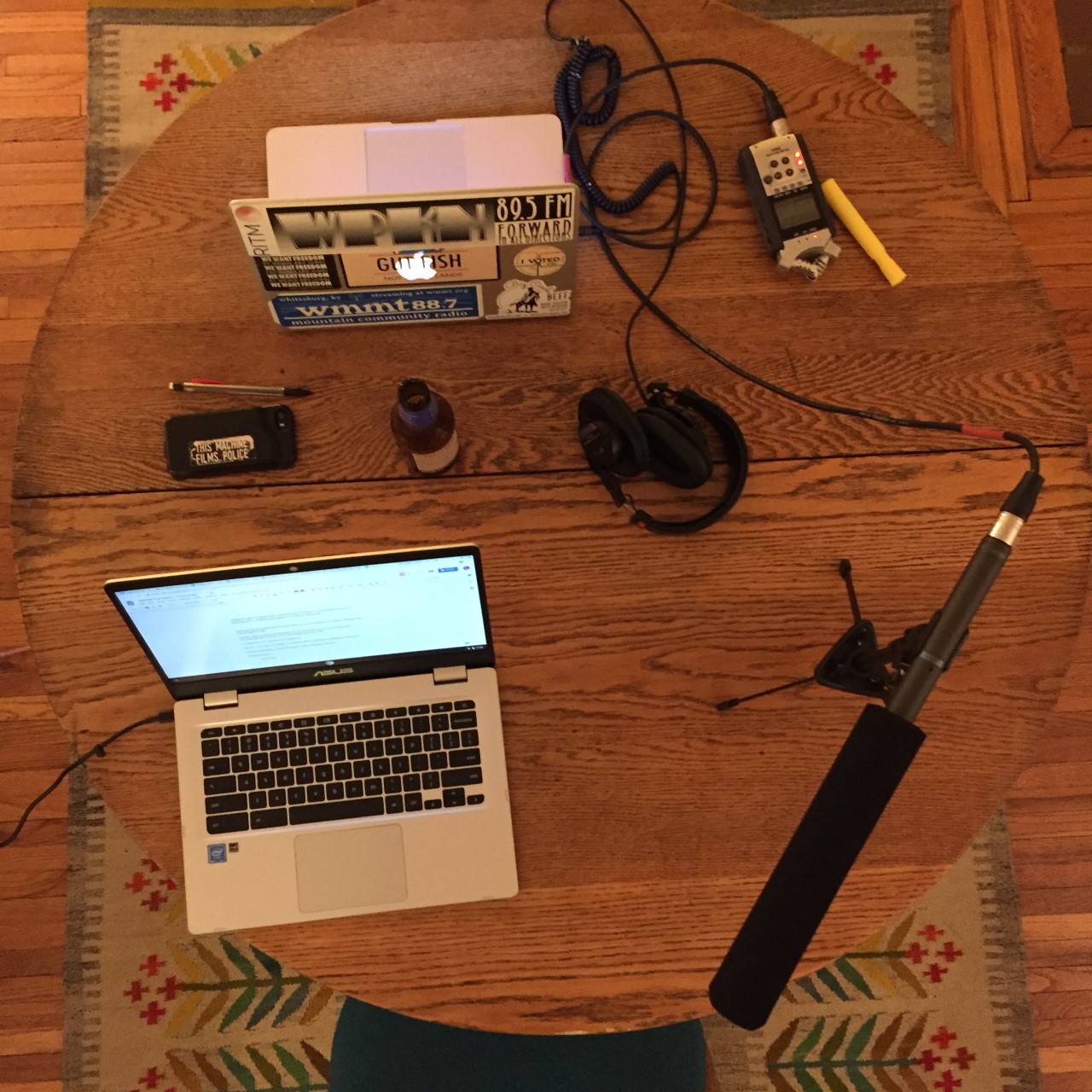 a bird's eye view of a circular wooden kitchen table. On top of the table are two laptops facing each other, hooked up to recorders and microphones.