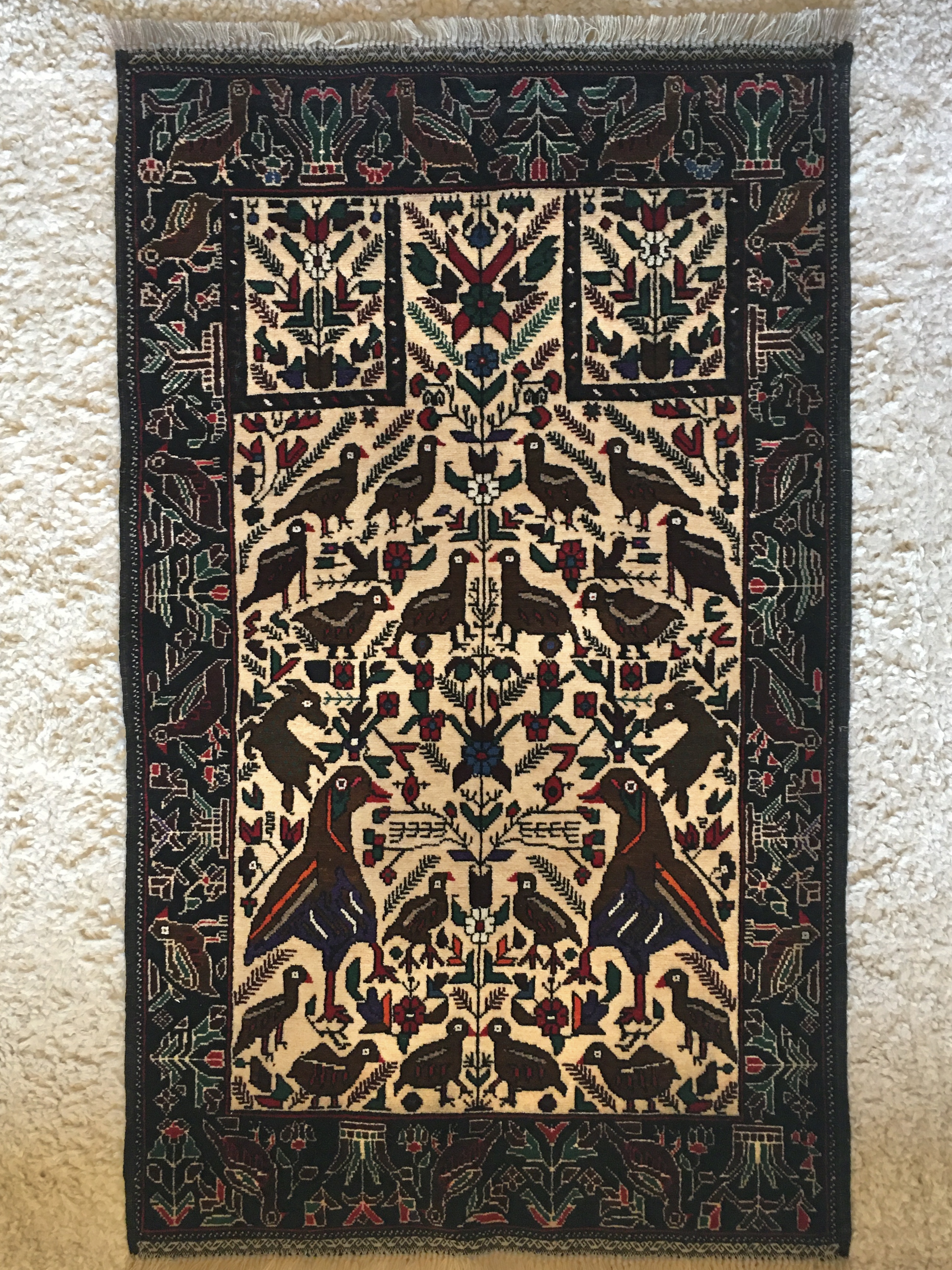 A prayer rug featuring many birds as well as fringed tree branches and other geometric floral patterns