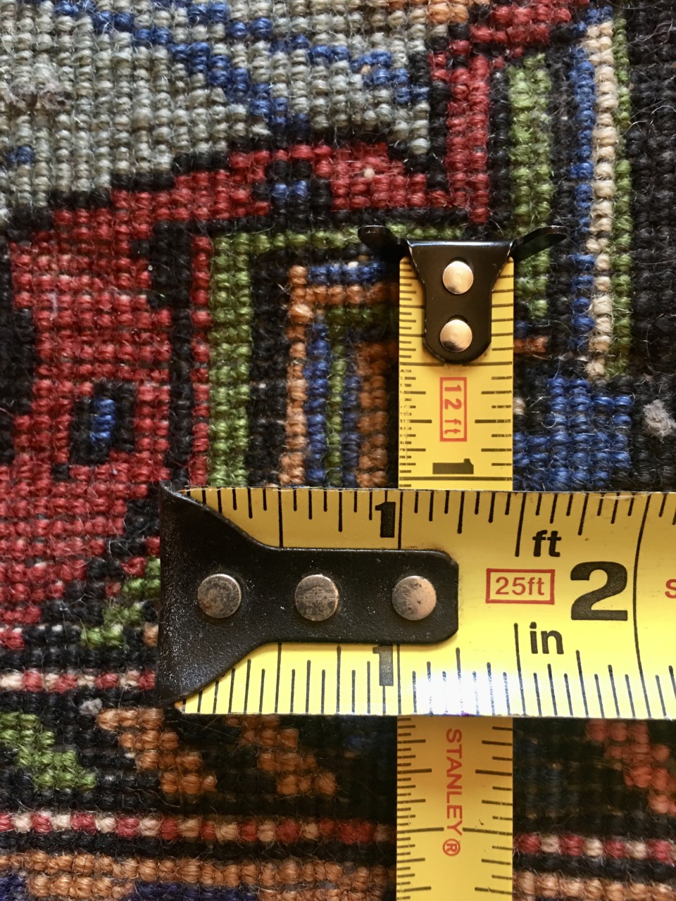 A detailed photo from the back of the Shirin Rug, taken so the knotting is more visible. A pair of measuring tapes are pictured, situated perpendicularly to demonstrate how many knots make up one square inch of space