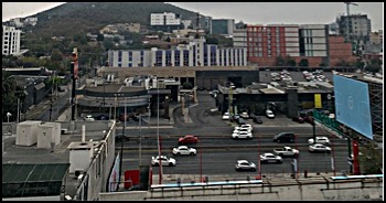 Major highway is the center of the photo, with businesses and city housing as a backdrop. Behind these buildings is a mist-covered mountain, and the weather is gray.