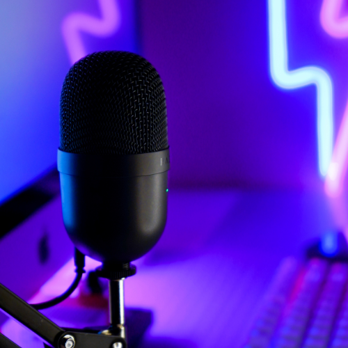 A podcast microphone in the foreground with a purple background and blue and purple neon lights.