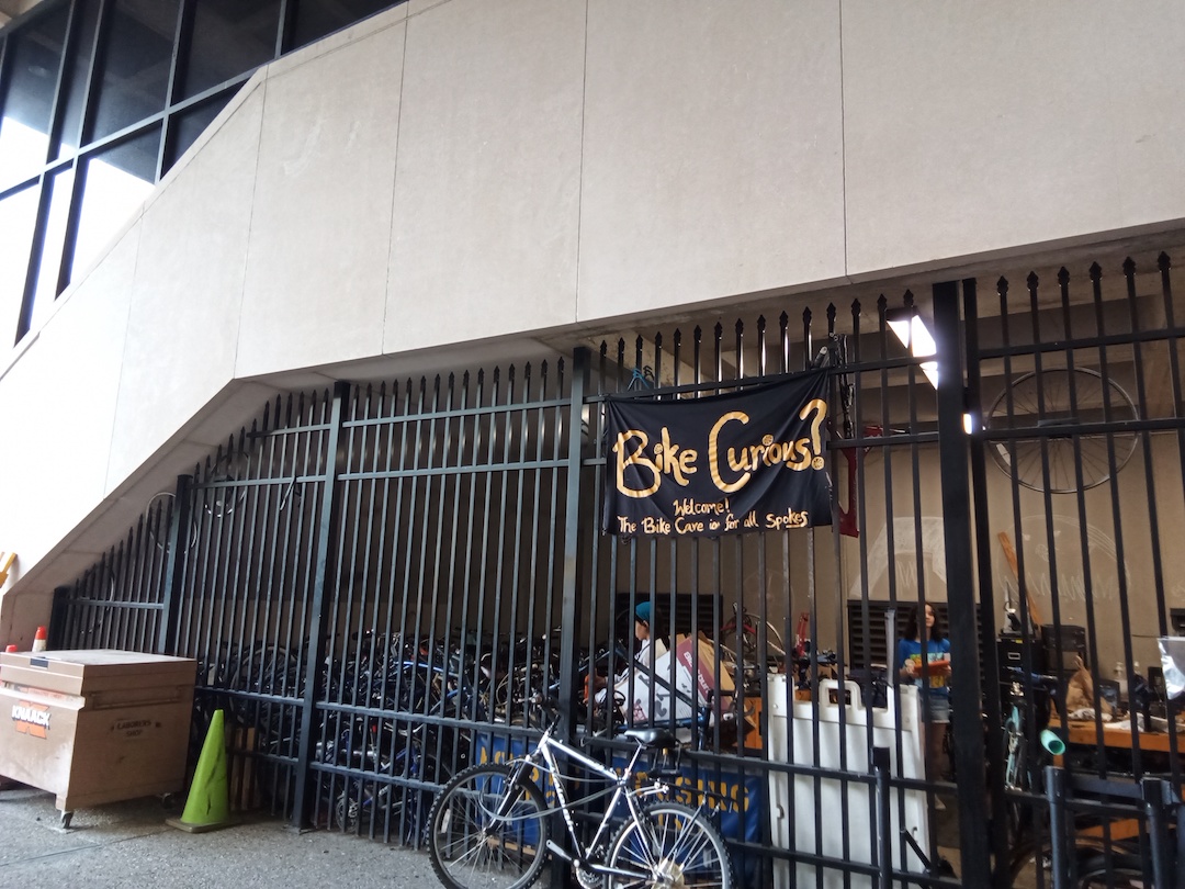 A bike leans against a black fence below a sign that reads, Bike Curious?
