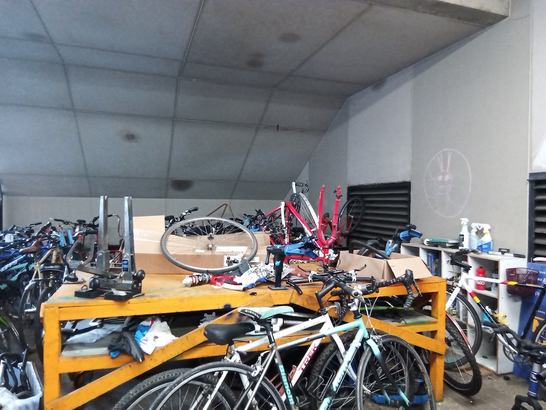 A large, messy workshop filled with bicycles, tools, and parts.
