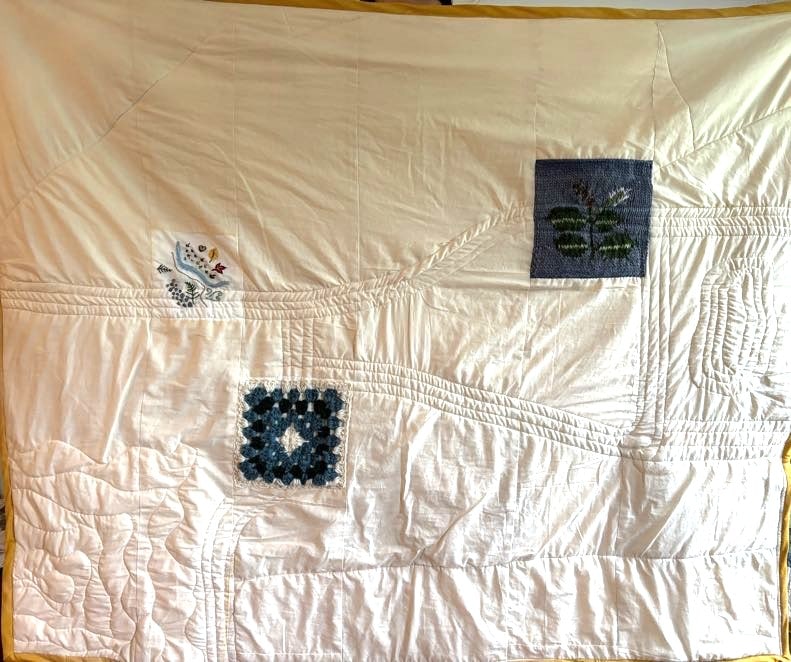 back side of quilt: white fabric with sewn lines and 3 small, multicolored squares