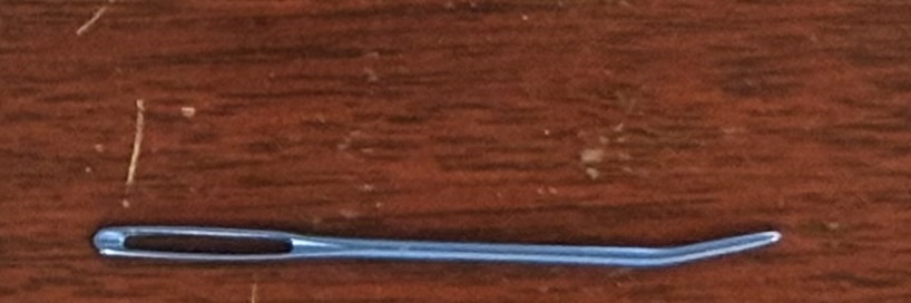 A blue, aluminum tapestry needle with a bent tip on a wooden background.