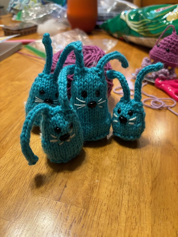 Four small blue knit bunnies of various heights and circumfrences sit together on a wooden table.
