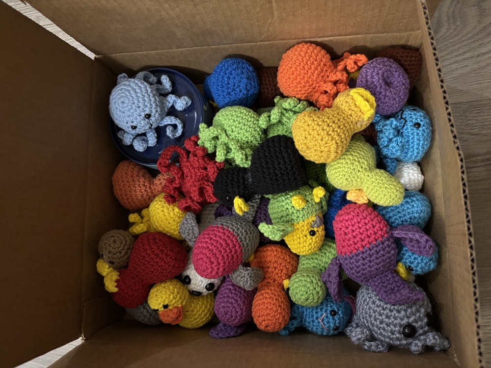 A cardboard box filled with crocheted plush creatures.