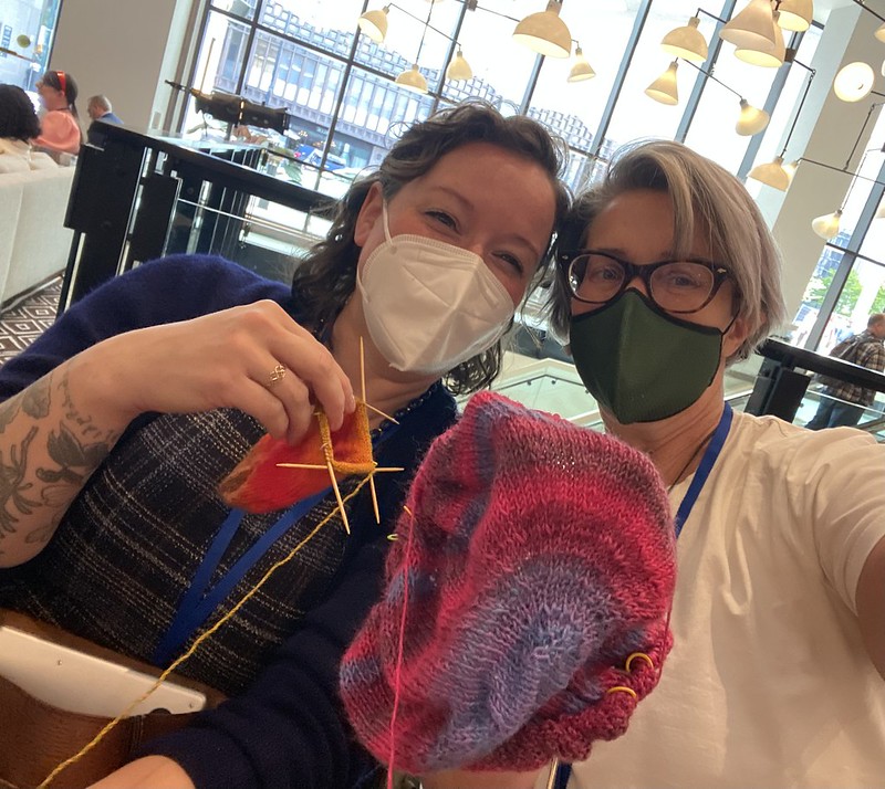 Margaret and Cagle hold up their current knitting projects at RSA 2024.