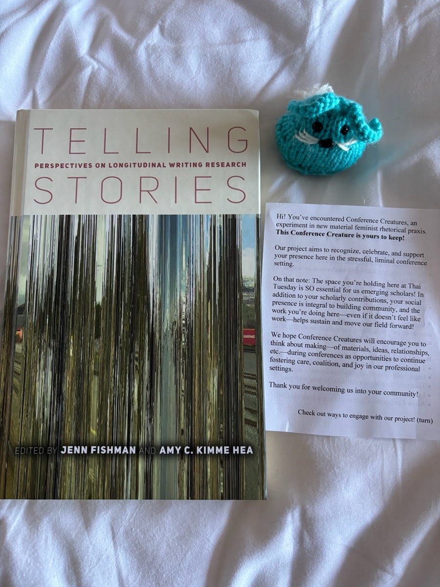 A blue knit bunny, a printed paper explaining Conference Creatures, and the book Telling Stories: Perspectives on Longitudinal Writing Research on top of a white background.