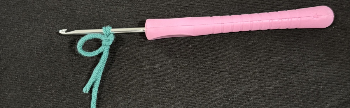 A purple crochet hook with one loop of blue yarn on top of a black background.