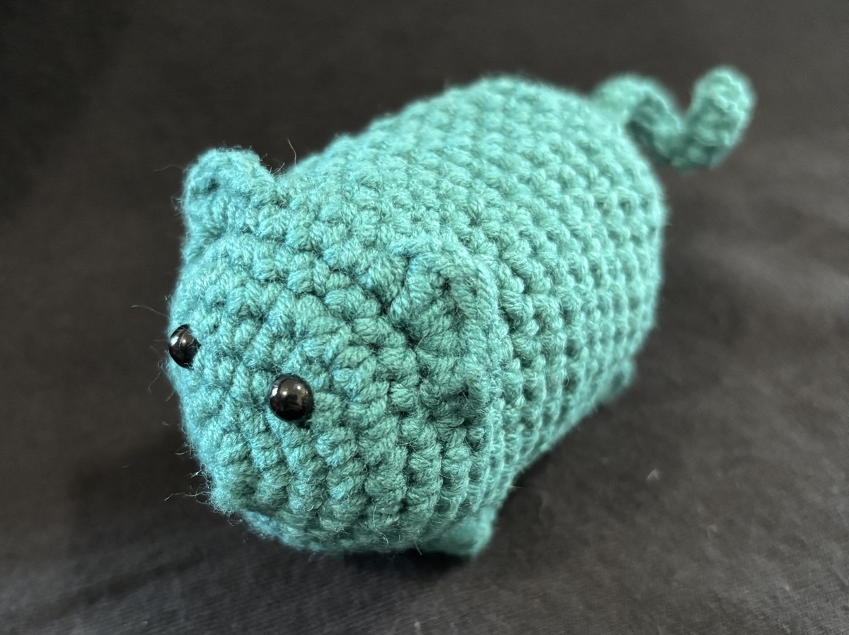 A completed blue crochet cat on a black background.