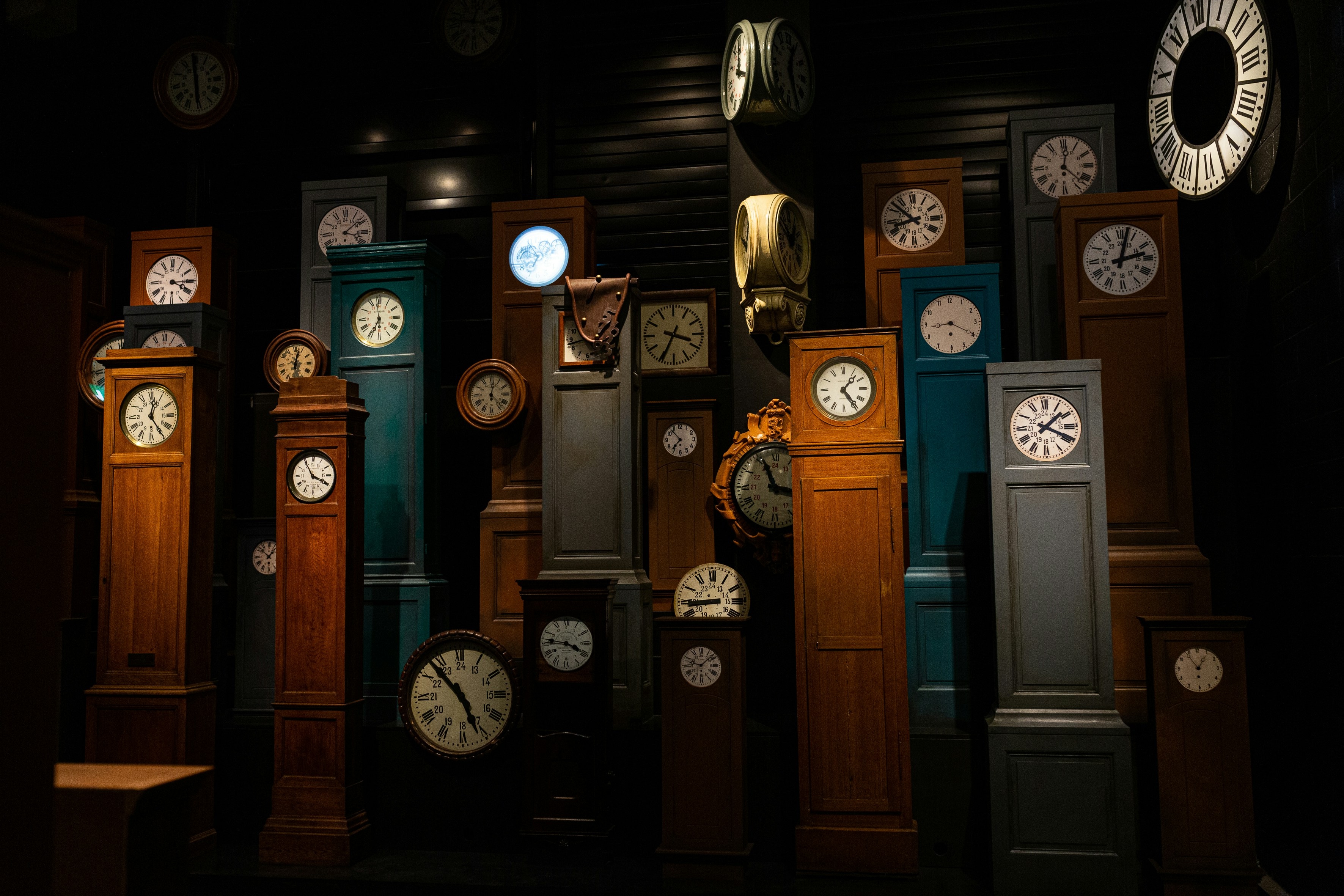 Many multi-colored grandfather clocks of various size stand next to each other.