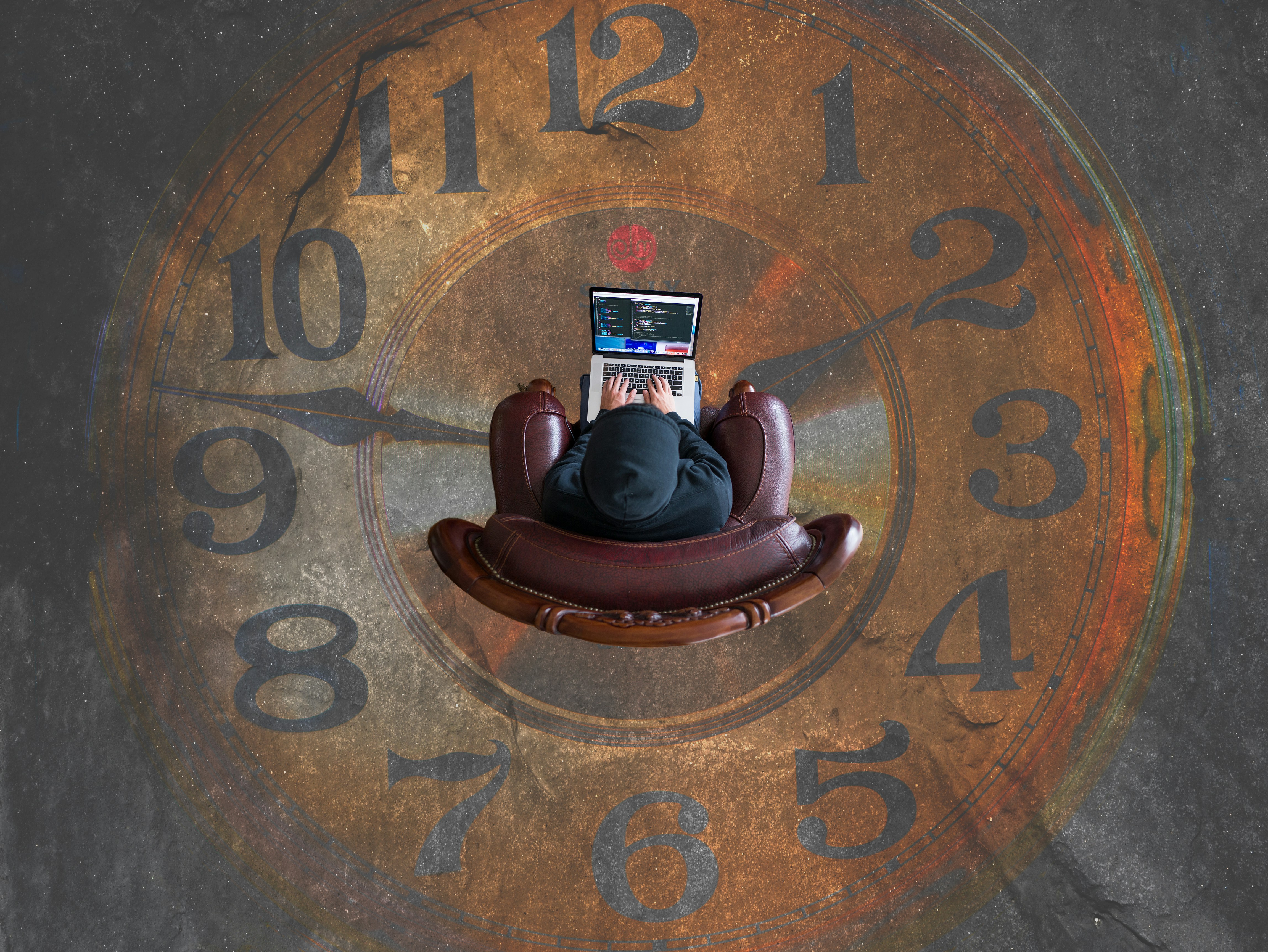 A person sitting in a chair working on a laptop. The chair sits in the middle of a large clock on the floor.