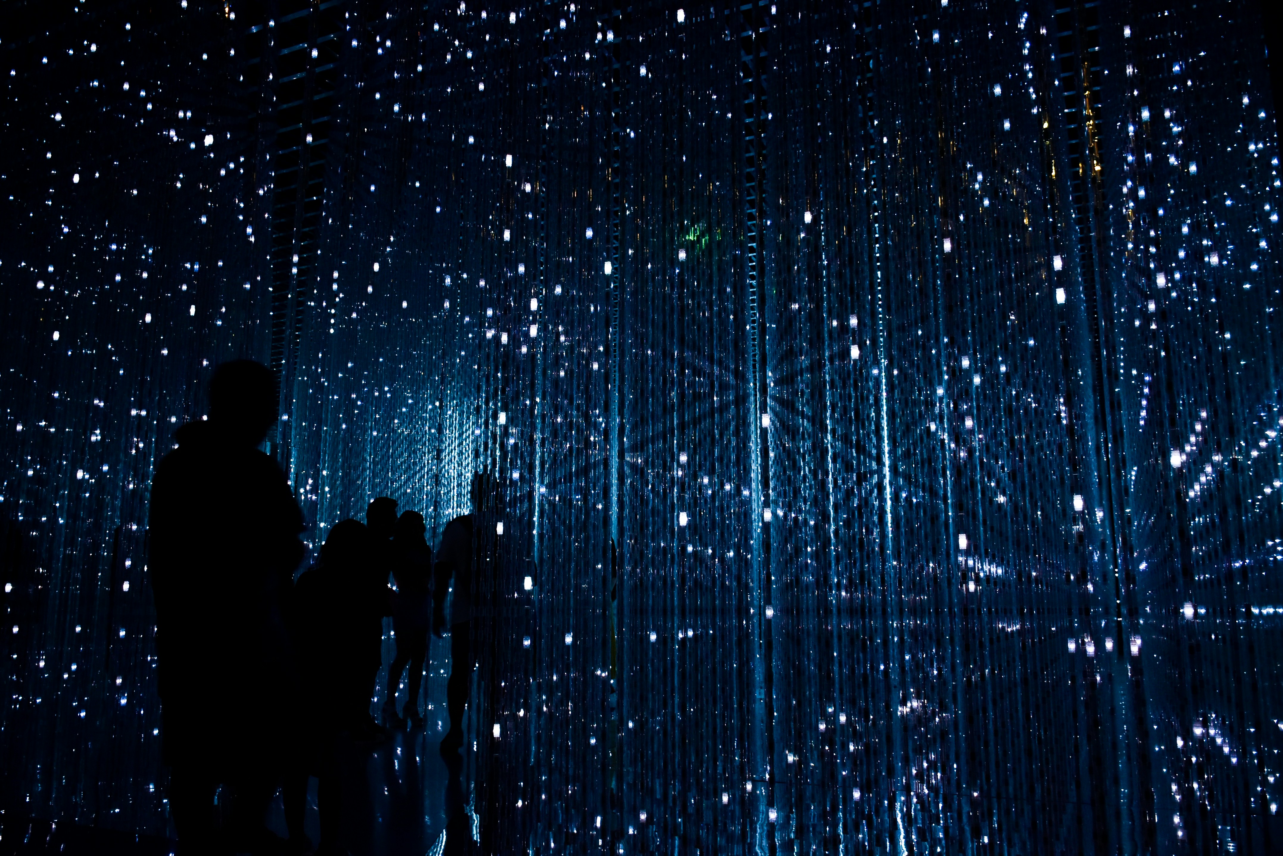 People standing close to each other in a blue hall of mirrors with spots of light all around.